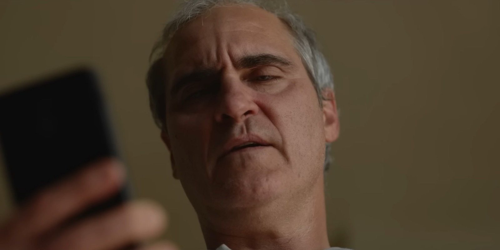 Joaquin Phoenix looking at a cell phone in Beau is Afraid