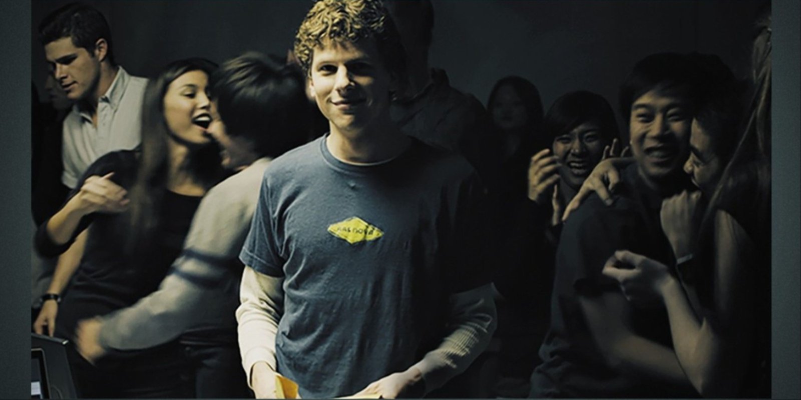 Jesse Eisenberg as Mark Zuckerberg on the main art for The Social Network with partygoers behind him.