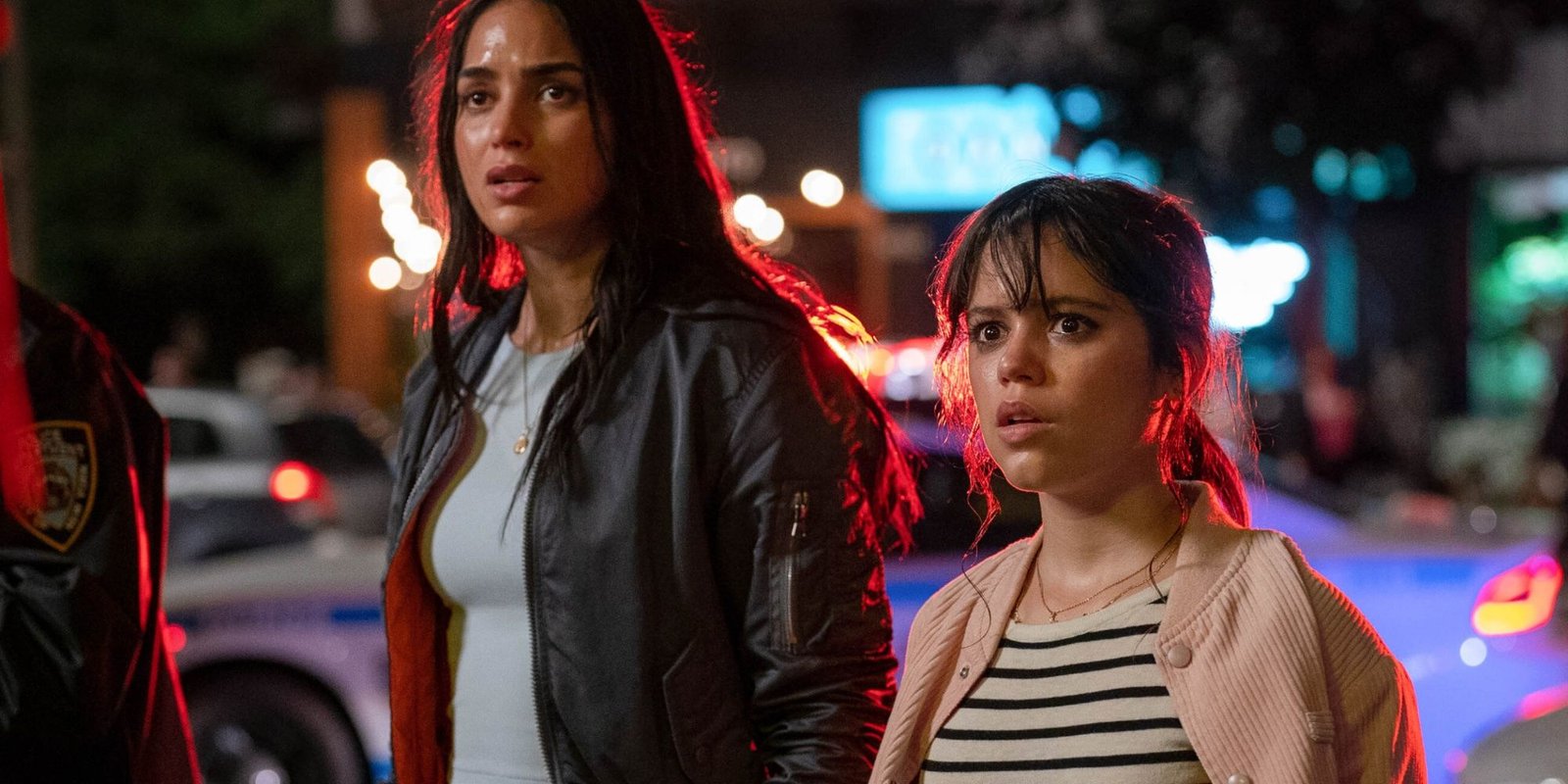 The two female protagonists of Scream VI stand amidst police cars, looking frightened.
