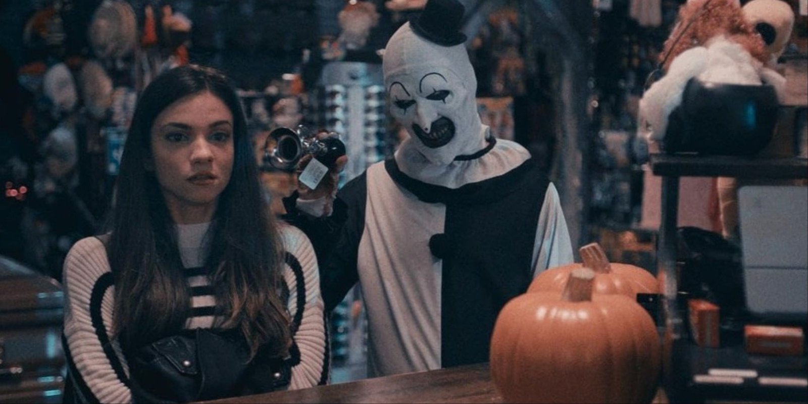 Art messing with Sienna in Terrifier 2 by signaling his horn right to her ear, with pumpkins and other Halloween decorations seen in the store.