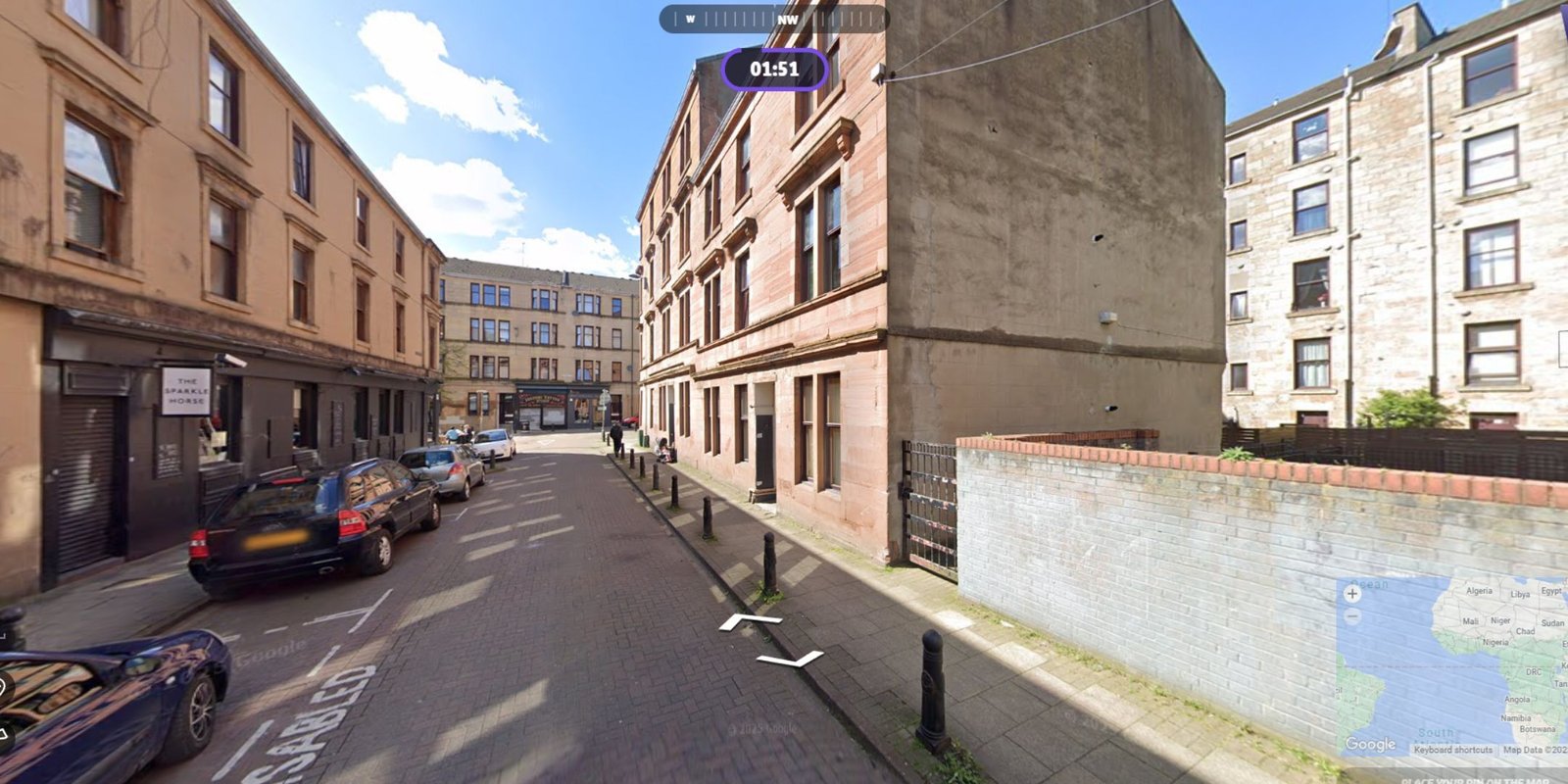 A screenshot from GeoGuessr, showing a random location from Google Maps. It is a street view of a street with cars parked 