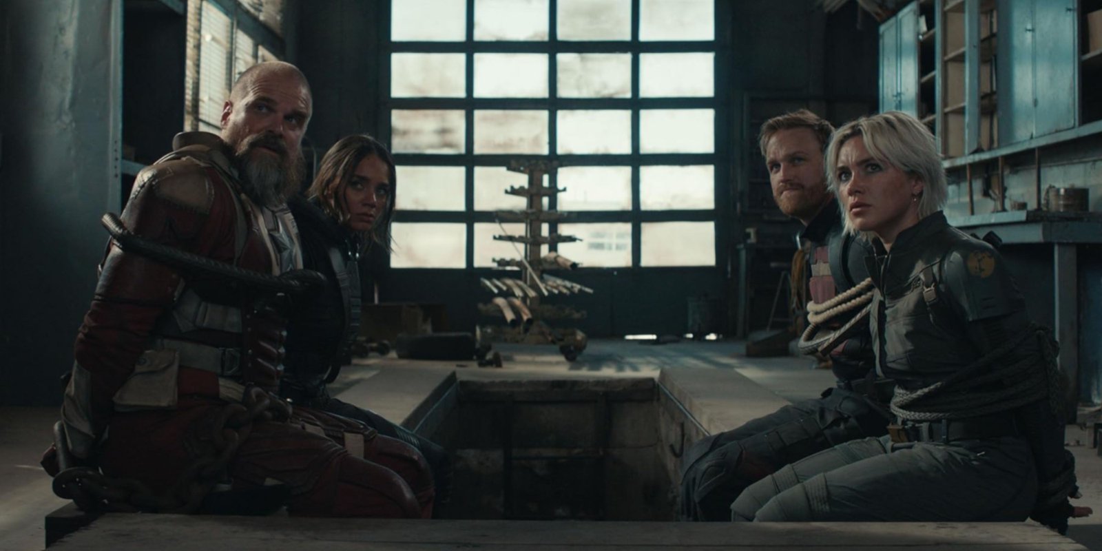 members of the thunderbolts cast tied up and sitting around a table.
