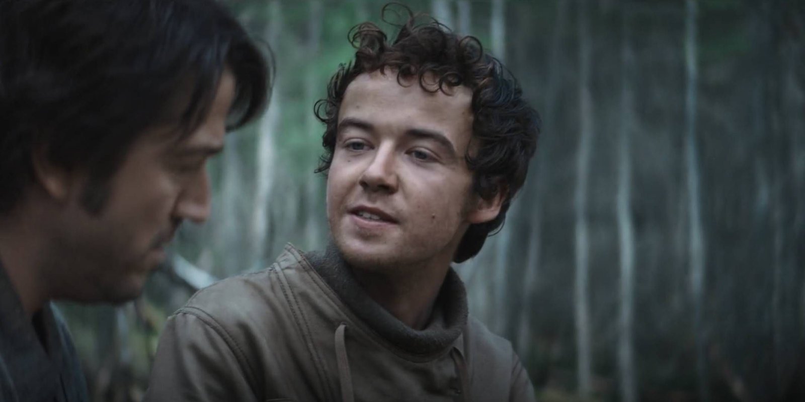 Karis Nemik talking to Cassian Andor with a smile among some trees on Aldhani in Star Wars: Andor.